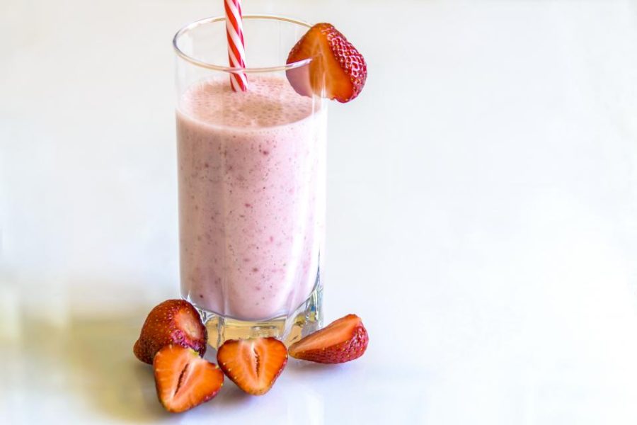 A pink strawberry smoothie in a tall glass with fresh strawberries