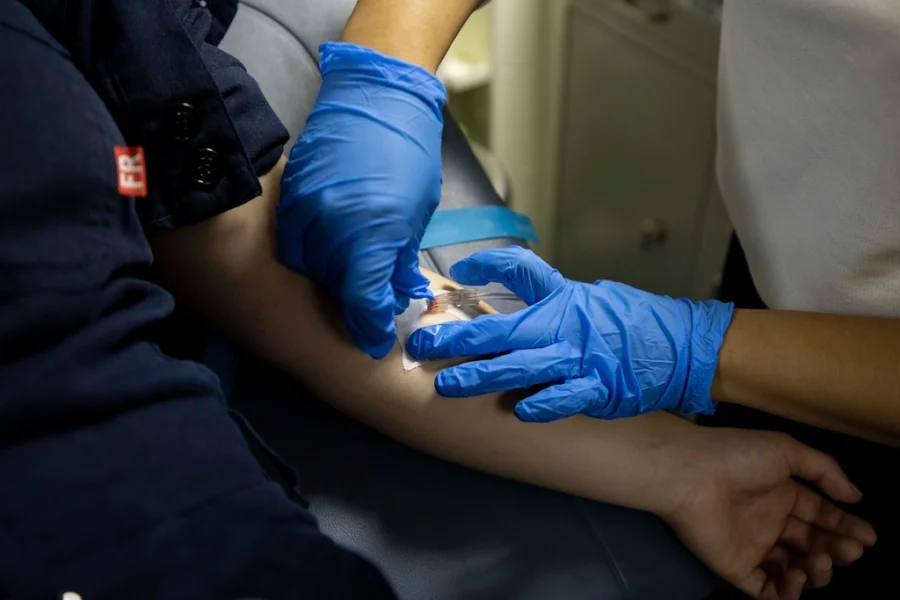 A clinician in blue gloves placing an IV line in a patient's forearm