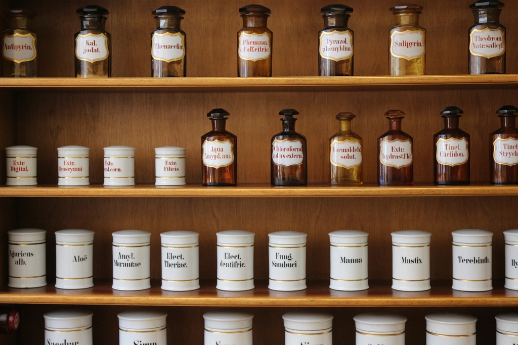 Old apothecary jars and bottles with Latin labels lined up on wooden shelves